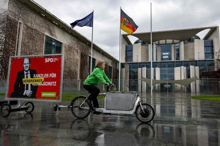 Una activista de Greenpeace en bicicleta tira de un remolque frente a la Cancillería alemana en Berlín con un cartel que representa al canciller alemán Olaf Scholz y un texto que dice «Canciller para la protección contra la combustión».