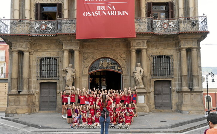 Unos niños y niñas se fotografían en la Casa Consistorial de Iruñea donde cuelga una camiseta gigante de Osasuna.