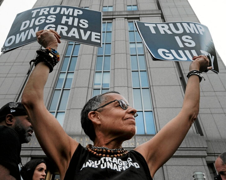 Una manifestante exhibe carteles que denuncian la culpabilidad de Trump.