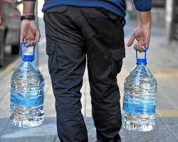 Un hombre lleva dos garrafas de agua embotellada. De los grifos capitalinos mana agua salada.