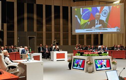 Los delegados, en sesión plenaria, atienden el discurso por videoconfenrencia del presidente ruso, Vladimir Putin.