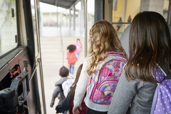 Unas niñas descienden de un autobús escolar.