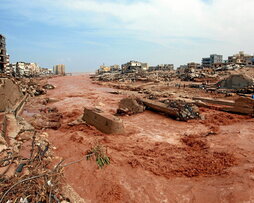 Varias personas observan la riada de agua y lodo y los destrozos causados en Derna.