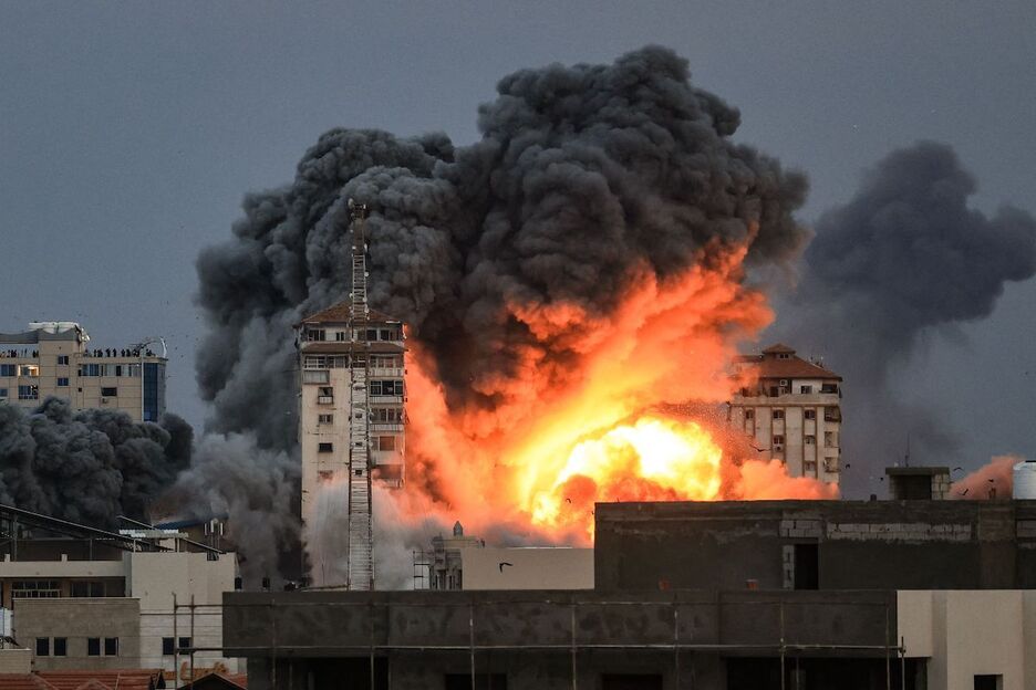Varias personas en una azotea observan cómo una bola de fuego y humo se eleva sobre un edificio en la ciudad de Gaza.