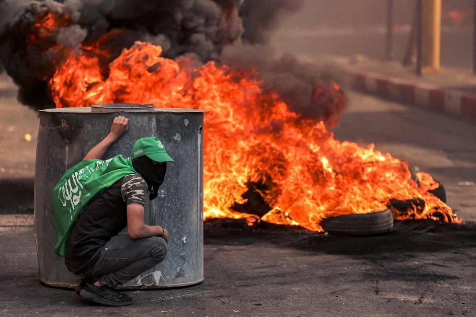 Un manifestante palestino enmascarado se cubre cerca de neumáticos en llamas durante los enfrentamientos con las fuerzas israelíes tras una concentración en solidaridad con Gaza en la ciudad de Hebrón, en la Cisjordania ocupada.