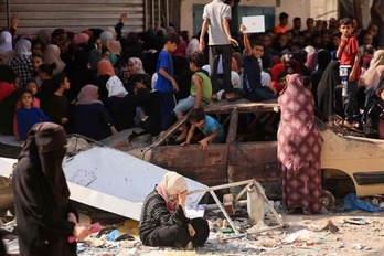 Palestinos hacen cola para comprar pan frente a una panadería parcialmente destruida por un ataque israelí en Nuseirat.