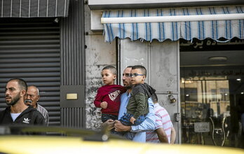 Un hombre con dos niños en brazos observa la comitiva que traslada los restos de uno de los menores muertos.