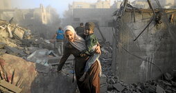 Una mujer con un niño sale del lugar atacado en el campo de refugiados de Al Maghazi.