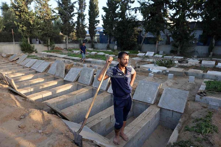 Un hombre descansa sobre una hilera de tumbas recién abiertas para la familia Hijazi, en Rafah.