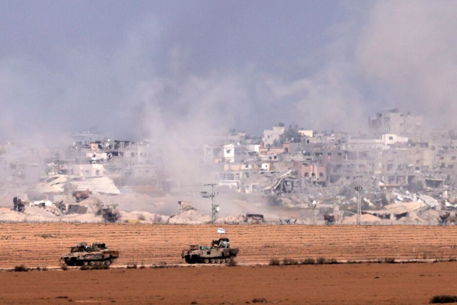 Vehículos blindados de transporte de tropas israelíes circulando a lo largo de la valla fronteriza mientras se eleva humo sobre el enclave palestino.