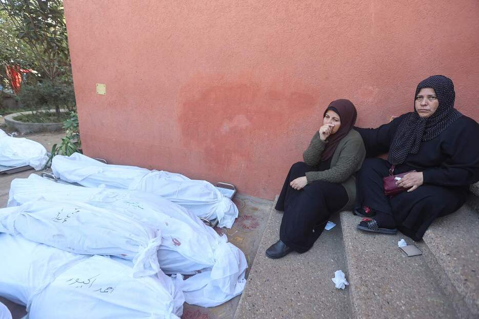 Varias mujeres sentadas junto a los cuerpos amortajados de familiares muertos tras ataques israelíes en el hospital Khan Yuniss Nasser.