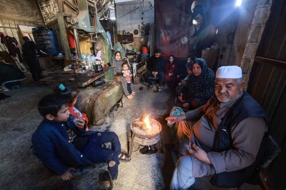 Miembros de una familia palestina que tuvieron que huir a Rafah se reúnen alrededor de una pequeña hoguera en el interior de un taller donde encontraron refugio temporal.