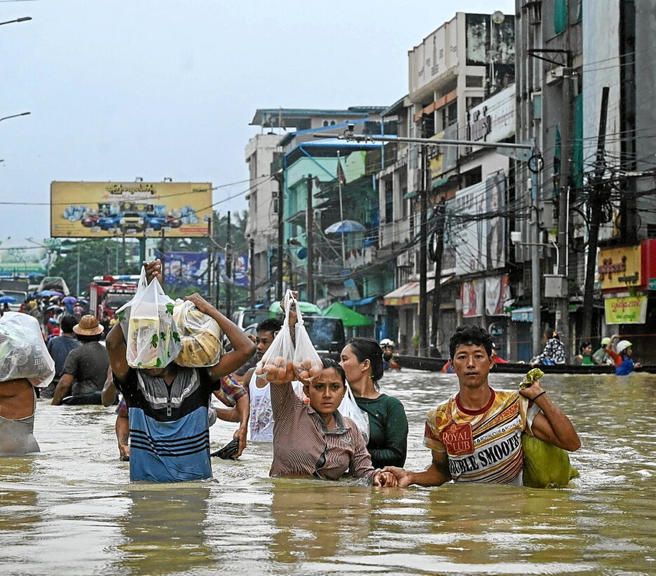Residentes cargan sus compras mientras caminan por una calle inundada en Bago, Myanmar.