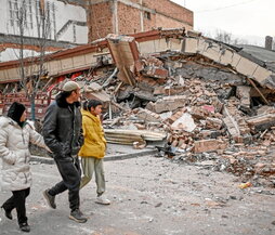 Una familia pasa junto a un edificio colapsado en Jishishan.