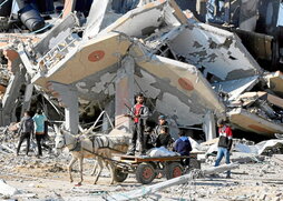 Palestinos en un carro, junto a un edificio destruido en el campo de refugiados de Al-Maghazi.