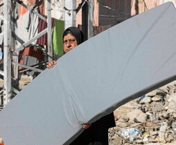Mujer palestina lleva un colchón ante los escombros de edificios destruidos en Rafah.