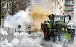 Un agricultor lanza heno sobre agentes de la policía antidisturbios belga, que responde con gas lacrimógeno.