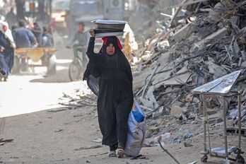 Una mujer palestina desplazada lleva sus pertenencias por una calle entre los escombros de las casas destruidas por los bombardeos israelíes en Khan Yunis, sur de Gaza.