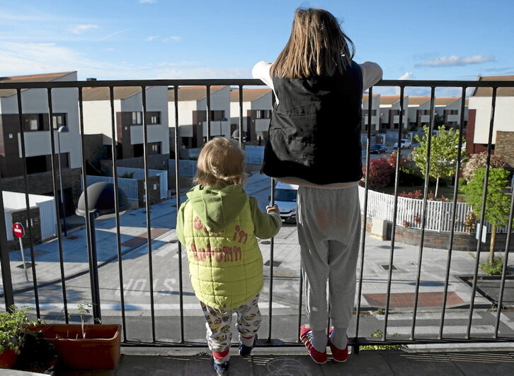 Dos txikis observan la calle, vetada por el confinamiento, desde el balcón de su hogar.