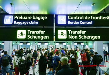 Los viajeros caminan al lado de señales recientemente instaladas que apuntan a las zonas de Schengen y no Schengen en el airopuerto internacional de Otopenis Henri Coanda, en Rumanía.