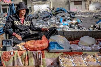 Un vendedor junto a su mercancía de paquetes de alimentos envueltos en su puesto en un mercado en medio de la destrucción en la ciudad de Gaza.