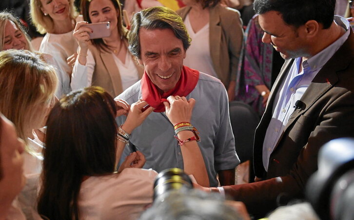 José María Aznar sonríe cuando le colocan un pañuelo al cuello durante el acto del PP en el Baluarte.