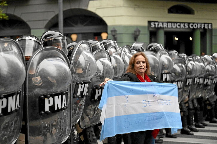 Una manifestante sujeta una bandera argentina frente a un cordón policial.