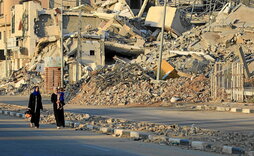 Palestinar desplazatuak al-Burej errefuxiatu gunean birrindutako eraikinen aurrean pasatzen.