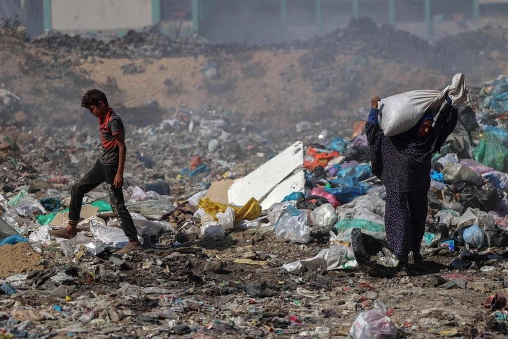 Palestinos buscan algo recuperable entre la basura en ciudad de Gaza.