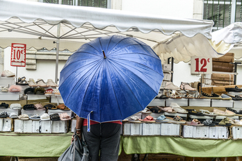 Un mercado estival, con sandalias en los puestos y clientes cobijados bajo el paraguas.La imagen se repite este verano de Euskal Herria a Normandia.