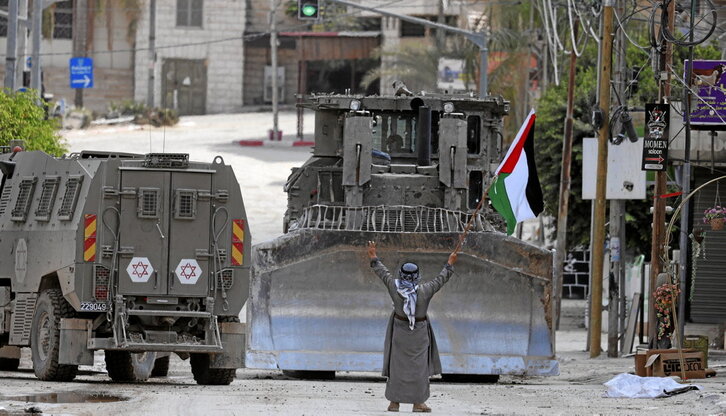 Un hombre levanta una bandera palestina y hace el signo de la victoria mientras blindados y excavadoras israelíes avanzan por una calle de Tulkarem.