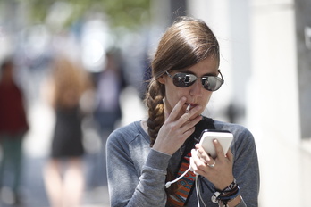 Una mujer fuma mientras consulta su teléfono móvil.