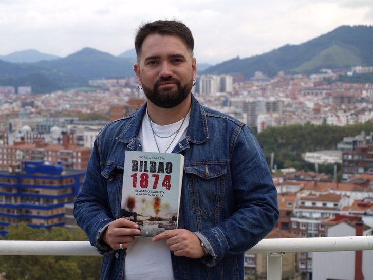 El historiador Gorka Martín posa con un ejemplar de su libro con la ciudad de Bilbo al fondo.