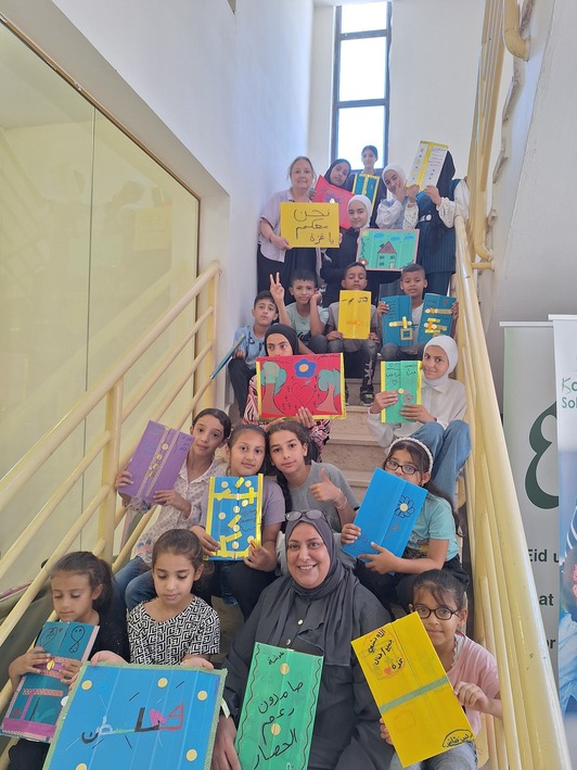 Educadoras, niños y niñas muestran sus trabajos en un taller en el campamento de Askar.