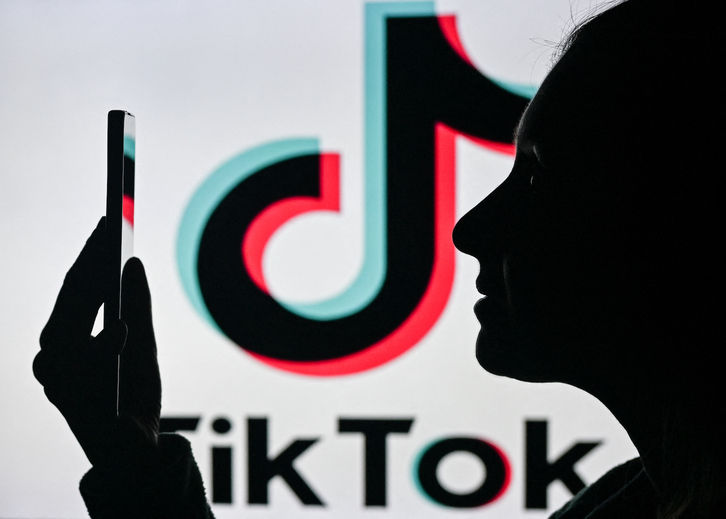 Imagen de una mujer con un teléfono móvil delante del logotipo de Tik Tok.