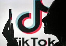 Imagen de una mujer con un teléfono móvil delante del logotipo de Tik Tok.