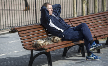 Gizonezko bat, txakurrek lagunduta, eguzkia hartzen. 