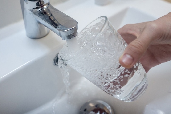 Una persona coge agua con un vaso en un grifo.