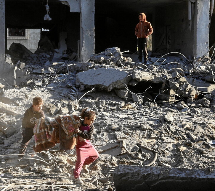 Dos niños recuperan una manta entre los escombros en Al-Maghazi.