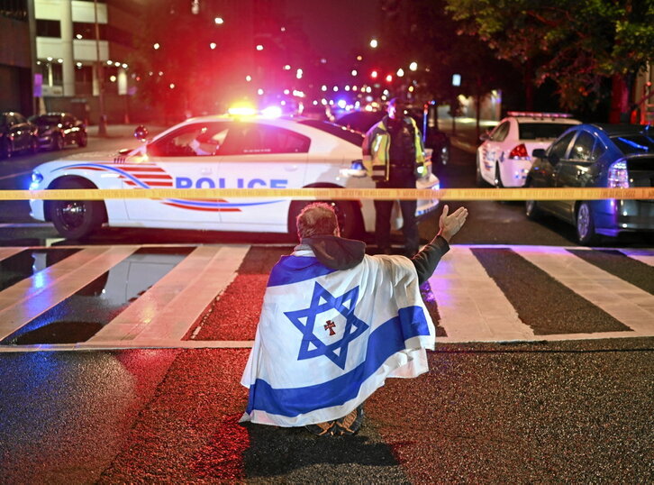 Israelgo banderan bildutako gizon batek keinu bat egin du Poliziaren aurrean tiroketa gertatutako inguruan.